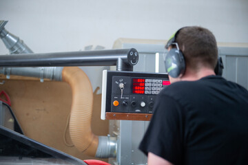 Ein Mann mit Geh&ouml;rschutz bedient eine digitale Steuerungseinheit einer Holzbearbeitungsmaschine in einer Werkstatt. Fokus auf das Display und die Technik, industrielle Umgebung.