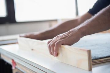 Ein Handwerker richtet ein Holzbrett auf einer Werkbank aus, Fokus auf die H&auml;nde und das Holz, helle Werkstattumgebung, keine Gesichter sichtbar.