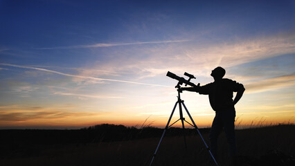 Fototapeta premium Silhouette of an amateur astronomer using telescope for observing stars, planets, Moon and other celestial objects.