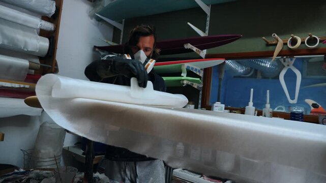 Man carefully paints detailed mask on surfboard in shaper workshop