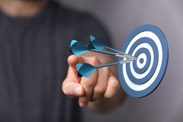 Image of hand pointing at darts hitting a dartboard bullseye representing precision target achievement and success. Great for business and goals