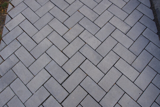 Close-up overhead view of a paved surface made of gray rectangular concrete or stone pavers set in a herringbone pattern.