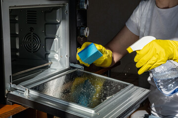 A person wearing yellow rubber gloves is cleaning an oven