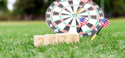 A fun gathering features a dartboard and three wooden blocks displaying the year 2026 on the grass, with American flags on the darts, capturing a festive holiday spirit