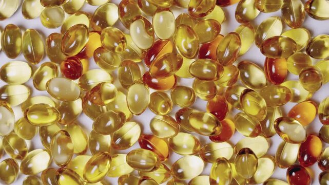 Top-down, close-up video of golden softgel capsules, like vitamin or fish oil supplements, slowly rotating on a turntable on white background showing concepts of healthcare, medicine, and nutrition.
