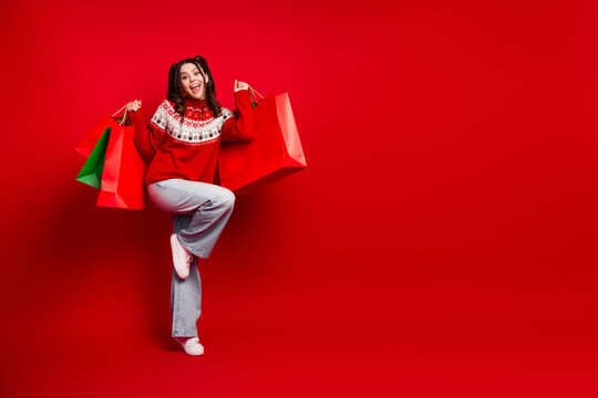 Happy young woman in red christmas sweater holds colorful shopping bags posed red background festive joy holiday spirit christmas season sale feature