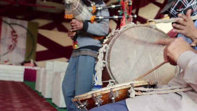 4K footage of Indian village musicians performing dhol and bagpipe during a marriage ceremony. Rhythmic drum beats and folk tunes create an authentic festive atmosphere in rural Uttarakhand.