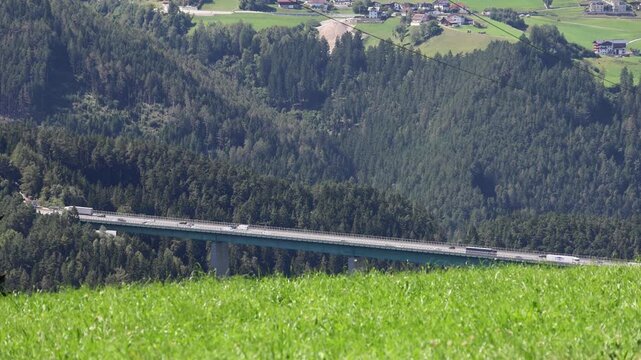 cars and trucks drive on a busy road in rural austria near italy (italian austrian border brenner pass) popular shipping route highway trucking delivery pollution car truck elevated alps mountains