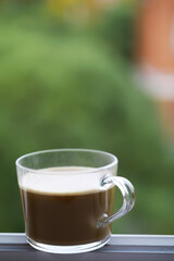 Glass Mug with Coffee on a Windowsill with Blurred Green Background