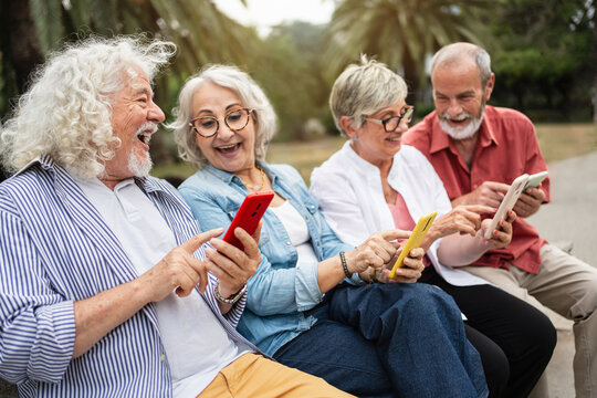 Happy modern senior people using mobile phone app together outdoors in city park, connected to technology - Powered by Adobe