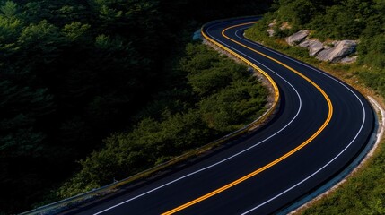 Fototapeta premium Scenic winding road through lush green forest with rocky outcrops under clear blue sky