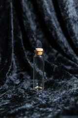 A small, tall, transparent glass bottle stands on a clean surface. It is completely empty, showcasing its slim shape and minimal design. 