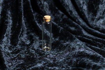 A small, tall, transparent glass bottle stands on a clean surface. It is completely empty, showcasing its slim shape and minimal design. 
