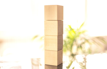 A tall stack of plain wooden blocks stands upright on a glossy table surface. Soft natural light fills the room, creating a calm and warm atmosphere