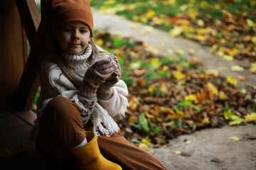 Cozy Autumn Moment: Child in Warm Clothes Enjoying Hot Drink with Fallen Leaves Background