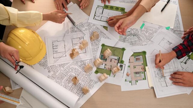Architect and safety engineer discussion about building construction use blueprint on table with architectural document, measurement tool and wooden block scatter around at modern office. Delineation.