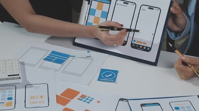 Two UX UI designers brainstorming mobile app wireframes in a modern startup office, showcasing creative teamwork, digital design