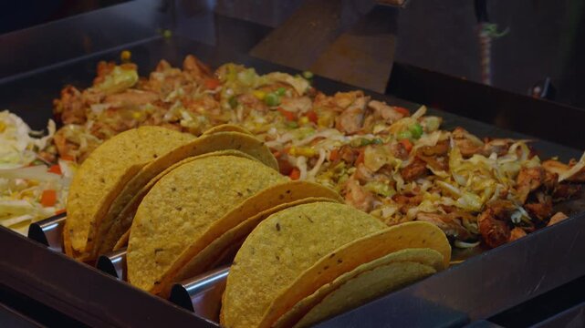 Fresh Hard-Shell Tacos Filled with Chicken, Cabbage, and Vegetables on Grill Station, Concept of Mexican Street Food Preparation