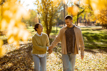 Joyful couple enjoying a sunny autumn day in the park while holding hands together