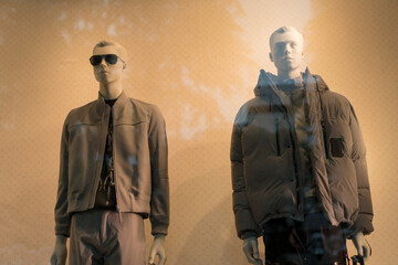 Two mannequins standing in store window display of men's casual clothing