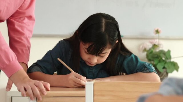 Asian girl writing or taking a note while teacher checking classwork. Caucasian teacher help happy student doing test or classwork while diverse student study in science lesson. Education. Pedagogy. - Powered by Adobe