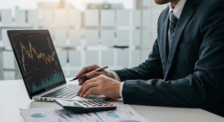 Focused businessman analyzing financial charts and market trends on laptop, planning investment strategy in modern office environment.