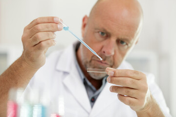 focused senior scientist pipetting biological solution on microscope slide