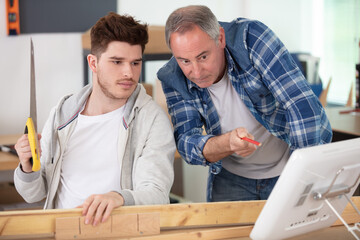 senior and craftsman apprentice together at laptop computer in workshop