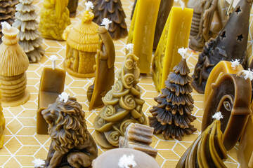Unique handmade candles shaped like trees, animals, and decorative structures displayed on a textured yellow surface in a cozy crafting space
