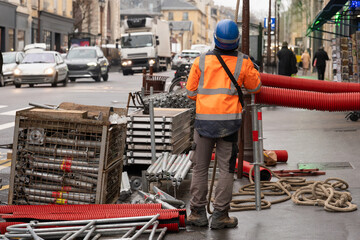 A worker in a hard hat sets up scaffolding on a busy street in the city center.