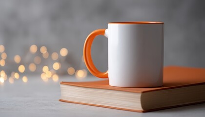 White Ceramic Mug With Blank Orange Handle Resting On A Book Surrounded By White Bokeh Lights, 11 Oz Size Mockup.
