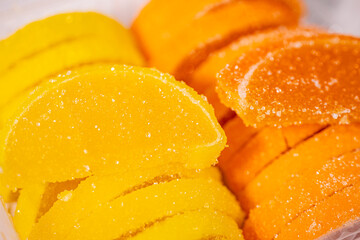 Bright yellow and orange jelly candies in the shape of citrus slices, coated in sugar and neatly packaged in a clear plastic tray. Bright colors and visible sugar texture.