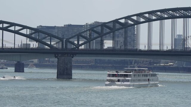 Tourist boat cruises on Rhein river in Cologne, Germany under Hohenzollern bridge with view of Kran house buildings at background