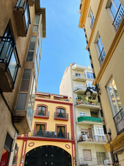 A view of a colorful, richly detailed street in the city center, flowers on balconies, and a wrought-iron lantern on the wall. Malaga, Spain, 2022.