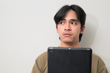 Portrait of handsome Young Asian Thai man using digital tablet computer against white wall thinking