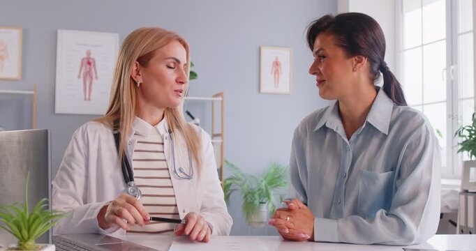 Young smiling friendly female doctor consulting woman patient sitting on workplace in examination room in medical clinic and giving recommendations in treatment in office. 4k video.