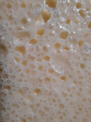 abstract surface the color of cream and caramel.
 close-up of the covered surface of orange-curd dessert with bubbles and craters. natural background
