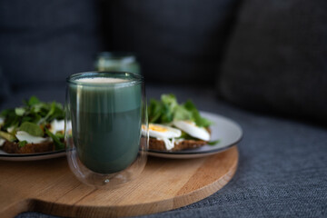 Coffee in a transparent glass sits on a wooden board beside plates of healthy food, showcasing a nutritious breakfast scene with vibrant colors and textures
