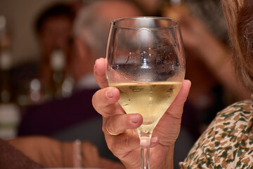 Hand raising a glass of white wine with condensation in a toasting gesture during a social celebration in an elegant setting