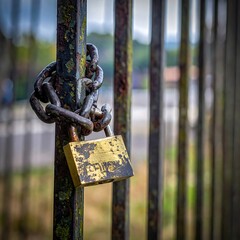 Close-up of a rusty gate secured with a chain and weathered padlock