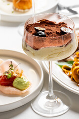 Elegant tiramisu dessert presented in a tall glass with layers of mascarpone cream, espresso-soaked ladyfingers, and a dusting of cocoa powder, garnished with blueberries