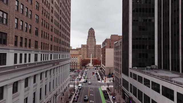 Aerial drone view of downtown Buffalo, New York, featuring a straight-on perspective of a city street lined with tall commercial buildings leading to the iconic Buffalo City Hall. The scene captures u