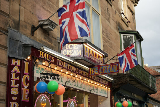 Union Jack Flags Fly Over Hall's Traditional Sweets And Ice Cream Shop Facade In Matlock Bath, Derbyshire, England, Under A Cloudy Sky.