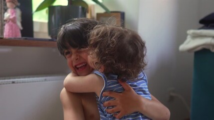 Toddler hugging older sibling tightly with joyful affectionate expression, warm family moment showing closeness, comfort, bonding, and genuine emotional connection between young children
