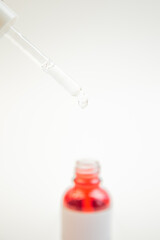 Close-up view of a dropper dispensing liquid above a vibrant red bottle, highlighting the skincare product's texture and application in a clean, minimalist environment