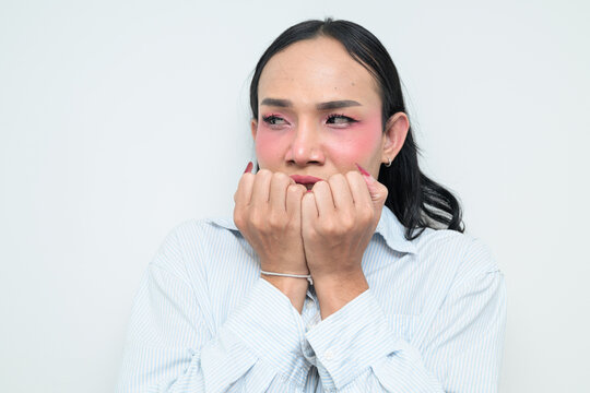 Portrait of a young scared Thai transgender person biting nails against white background