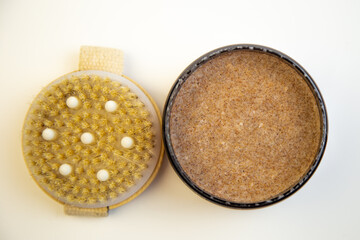 Round container of natural body scrub next to an exfoliating brush, highlighting organic skincare essentials for self-care and pampering experiences