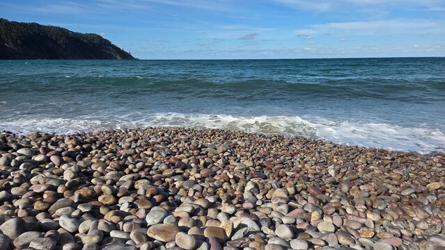 Scenic ocean view with rocky beach and distant cliffs under clear sky. Horizontal banner. Copy space. Travel, vacation concept