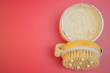 Body scrub in silver container paired with a natural bristle brush on a bright pink backdrop, emphasizing indulgent self-care and beauty routines
