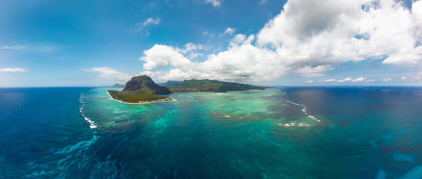 Aerial panorama of Le Morne Brabant peninsula with turquoise lagoon and underwater waterfall. Breathtaking view of coast with luxury beach resorts at the foot of iconic mountain in Mauritius